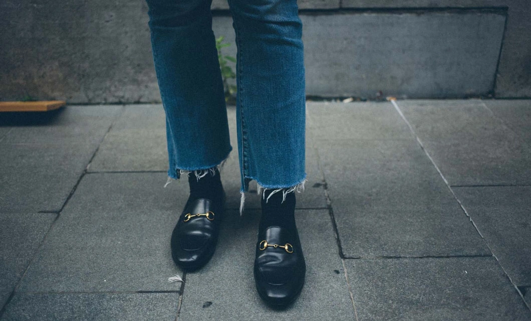 A person stands wearing black shoes and jeans, showcasing a casual yet stylish outfit