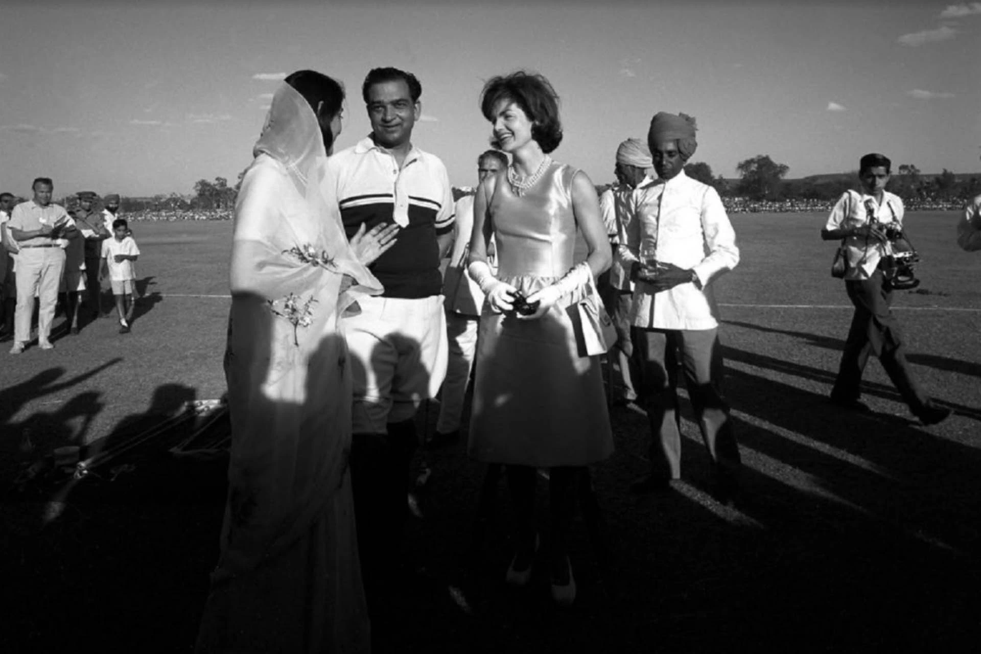 A woman in a white dress speaks with a man in a suit, echoing Jacqueline Kennedy’s meeting with the Maharaja and Maharani of Jaipur