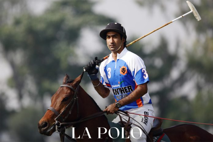 Polo player in action on horseback, wearing team jersey with a mallet in hand.