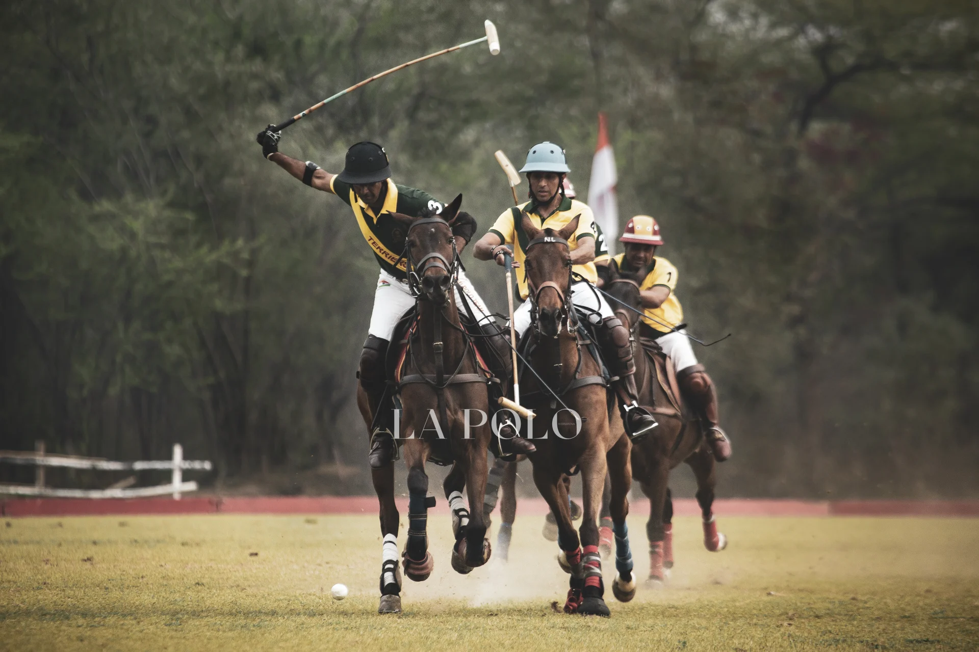 Three polo players, riding fast on horses, compete fiercely on a grassy field, with mallets raised for a striking shot.