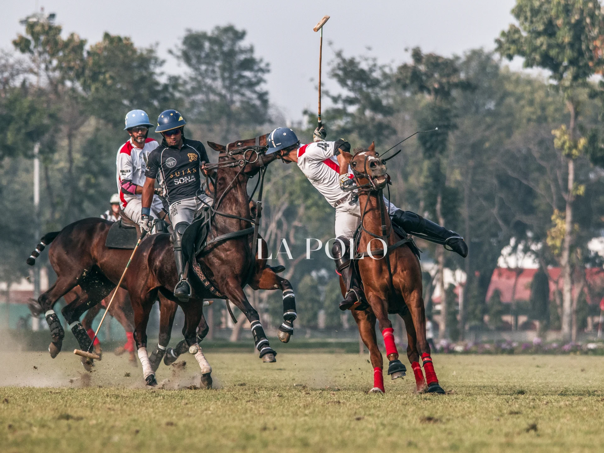 Action-packed polo match with two players striking the ball, while another rider approaches in a lush green field.