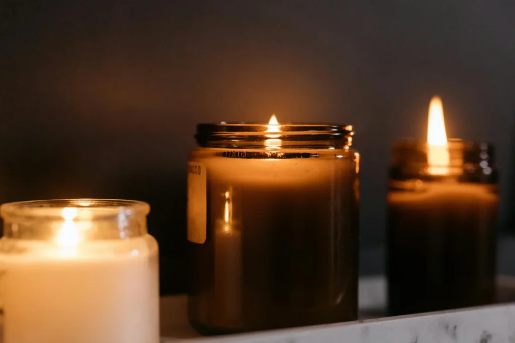 Three candles flicker gently on a shelf, providing a tranquil ambiance with their warm, glowing flames