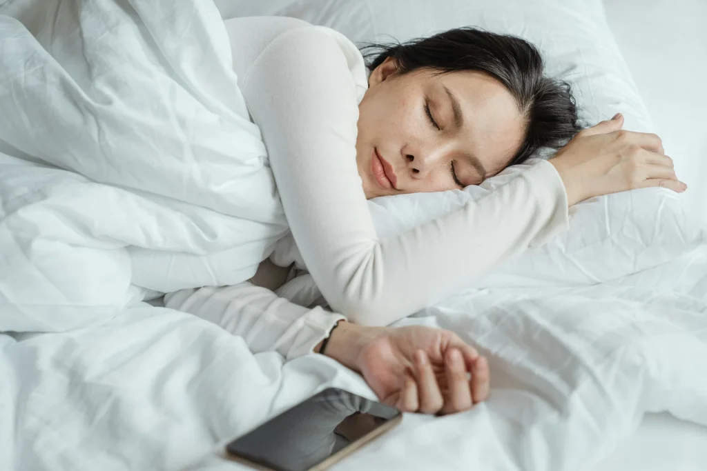  A woman peacefully sleeping in bed, her phone resting beside her on the pillow