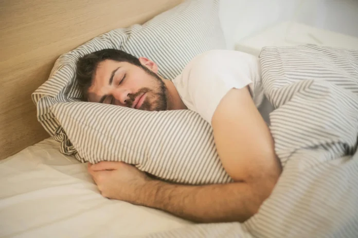 A man peacefully sleeping in bed, resting his head on a soft pillow, surrounded by cozy bedding