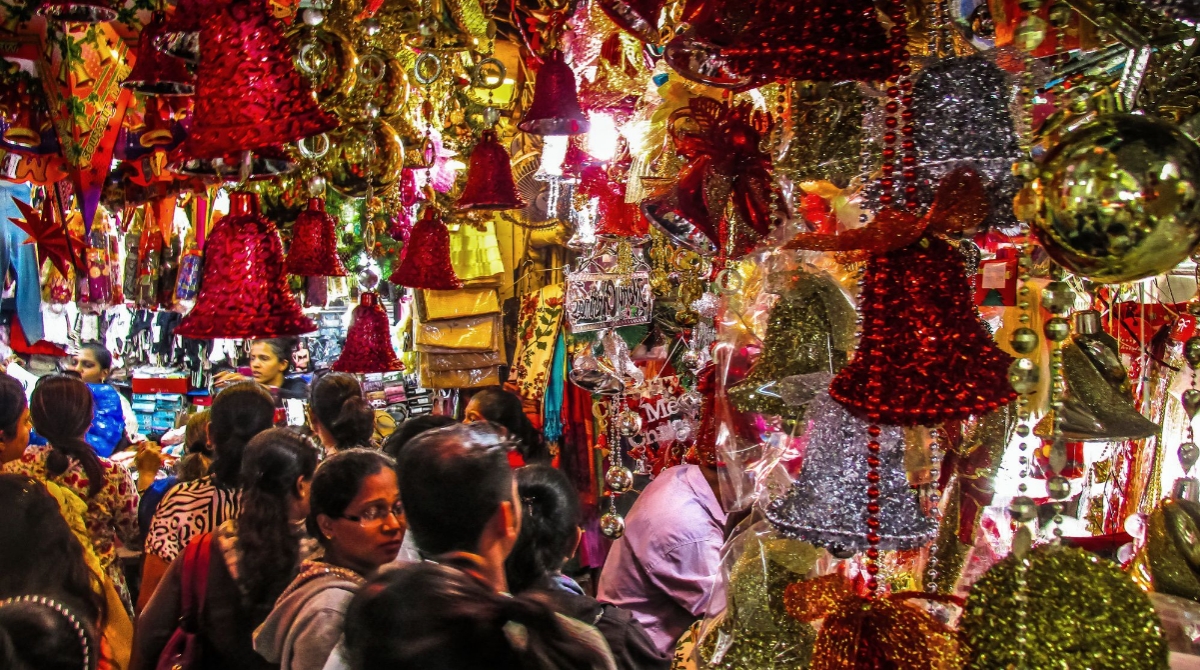 A crowded market with many people surrounded by colorful Christmas decorations, including red and silver bells, and other festive ornaments hanging from above.