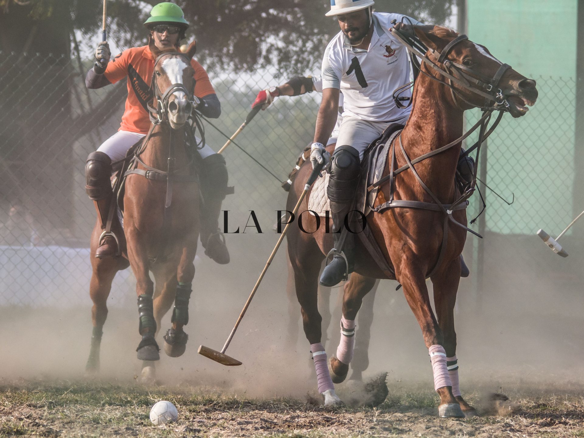 Two men engaged in a polo match, riding horses and competing on a dirt field.