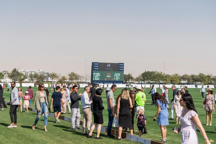 Excited crowd at an outdoor Polo sports event, watching the game with a large scoreboard in the background – energetic live match atmosphere.