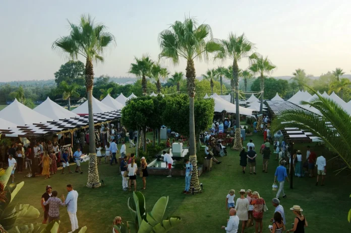 A diverse crowd of people enjoying an outdoor event, engaged in conversation and activities under a clear sky.